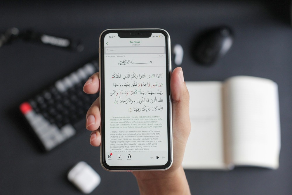 Person holding smartphone displaying Quran Surah An-Nisaa with Arabic and Indonesian translation, Islamic app for digital reading